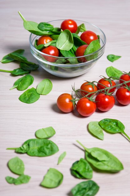 Concetto di cibo sano - primo piano di insalata con spinaci e pomodori su sfondo tavolo in legno