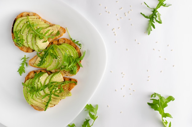 Concetto di cibo sano. Toast con avocado, gamberi e rucola su sfondo bianco. Vista dall'alto, piatto.