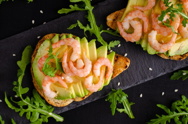 Concetto di cibo sano. Toast con avocado, gamberi e rucola. Vista dall'alto, piatto