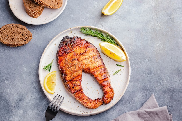 Concetto di cibo sano. trancio di salmone alla griglia con limone, rosmarino servito su piatto bianco su pietra grigia