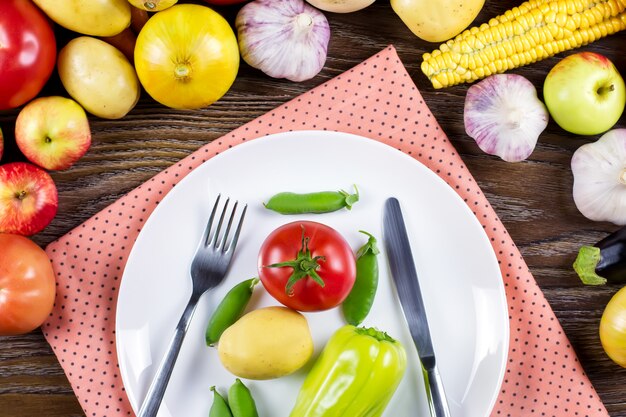 Concetto di cibo vegan crudo. Verdure crude, piatto con posate e tovagliolo su fondo in legno