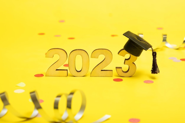 Concetto di classe 2023 Numeri 2023 con cappuccio graduato nero su sfondo giallo