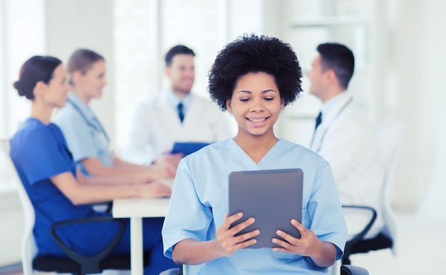 concetto di clinica, professione, persone e medicina - medico femminile felice con computer tablet pc su un gruppo di medici riuniti in ospedale