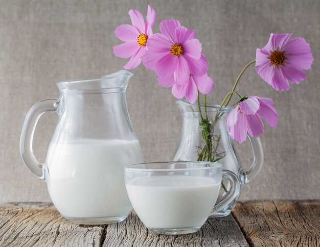 Concetto di colazione. Tazza di latte sulla tavola di legno con i fiori