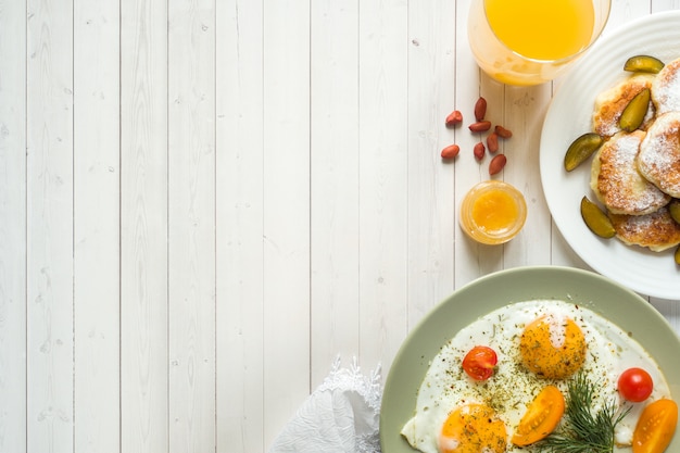 Concetto di colazione. Uova fritte, frittelle di ricotta, prugne e farina d'avena con latte, succo d'arancia sul tavolo