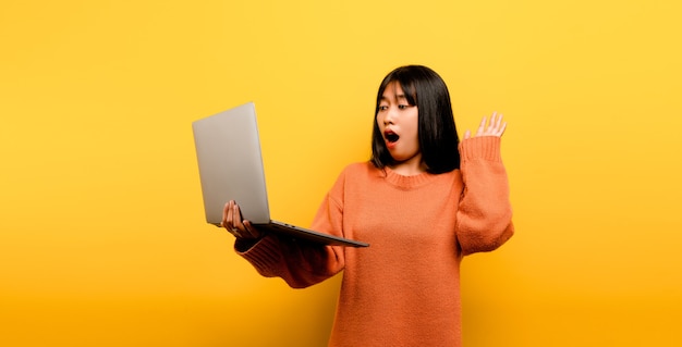 Concetto di comunicazione online ragazza asiatica usa il computer portatile a casa giallo studio foto È felice di trascorrere il suo tempo libero online mentre chatta con gli amici sui social network, fa shopping o lavora online.