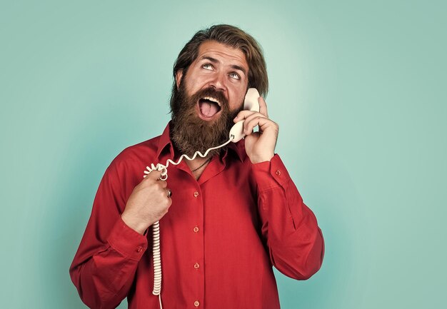 Concetto di comunicazione uomo barbuto in camicia chiamata al telefono ragazzo casual durante la conversazione hipster emotivo con capelli lunghi e baffi maschio che parla al telefono retrò