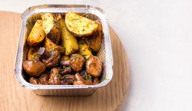 Concetto di consegna del cibo. Patate fritte con funghi in un contenitore.