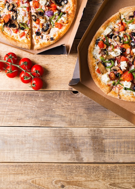 Concetto di consegna. Pizza vegetale in scatola di cartone aperta sul tavolo di legno, copia spazio, verticale