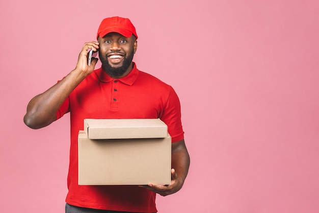 Concetto di consegna. Uomo nero di consegna afroamericano che trasporta il pacco. Utilizzando il telefono.