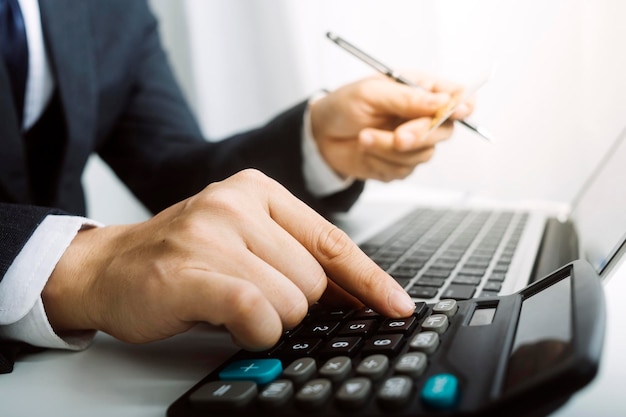 Concetto di contabilità aziendale Uomo d'affari che utilizza la calcolatrice con il budget del computer portatile e la carta di prestito in ufficio
