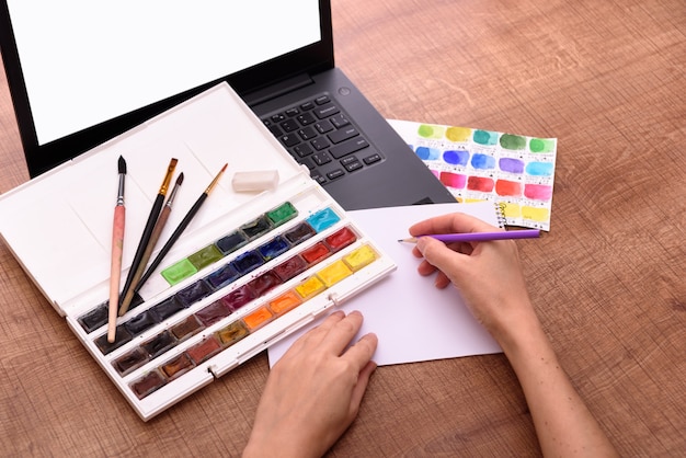 Concetto di copertina del corso di disegno online con foglio per laptop di colori di carta e pennelli su de...