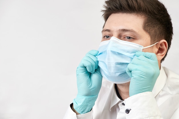 Concetto di coronavirus, uomo che indossa la mascherina medica protettiva sul muro bianco