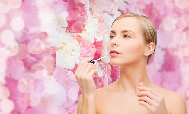 concetto di cosmetici, salute e bellezza - bella donna con lucidalabbra rosa