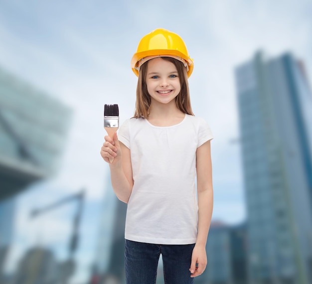 concetto di costruzione e persone - bambina sorridente in casco protettivo con pennello