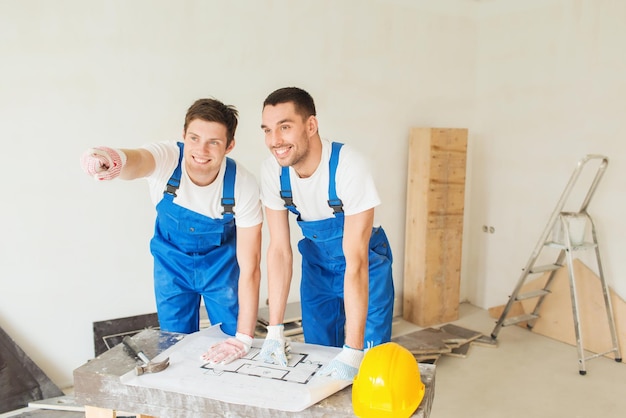 concetto di costruzione, lavoro di squadra e persone - gruppo di costruttori sorridenti in elmetti protettivi con progetto all'interno