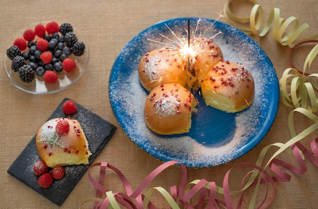 Concetto di cucina casalinga Pane al latte dolce fresco biologico fatto in casa ripieno di crema e decorato con frutti di bosco su piatto blu con luci scintillanti