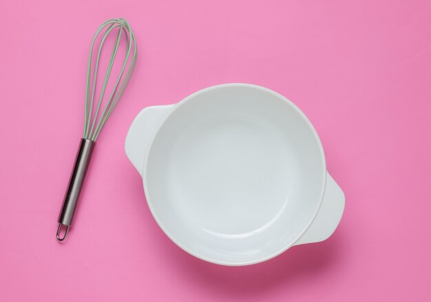 Concetto di cucina. Ciotola bianca vuota con frusta su sfondo rosa per studio. Vista dall'alto.