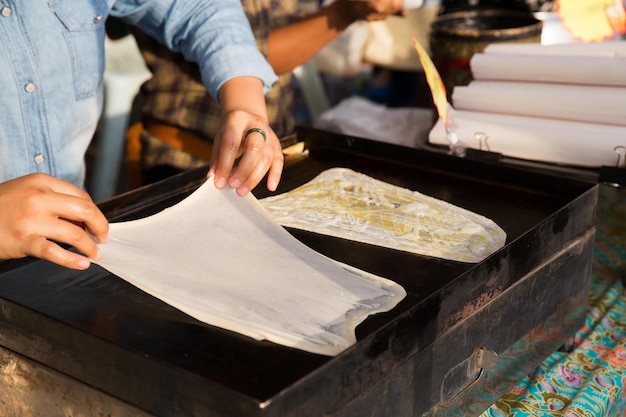 concetto di cucina, cucina asiatica, persone e vendita di cibo - donna che cucina frittelle di roti sul fornello del mercato di strada