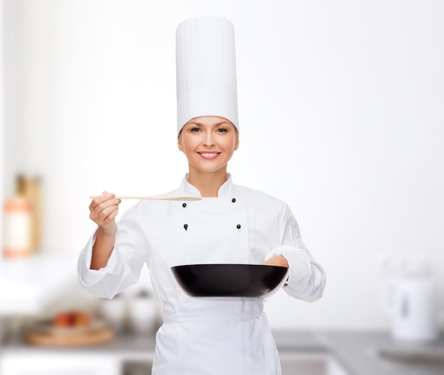 concetto di cucina e cibo - chef femminile sorridente con padella e cucchiaio di degustazione di cibo