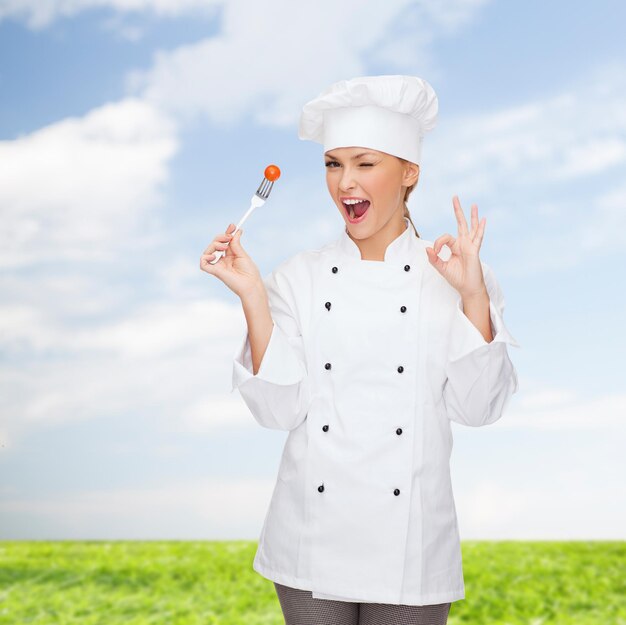 concetto di cucina e cibo - chef femminile sorridente, cuoco o fornaio con forchetta e pomodoro che mostra il segno giusto