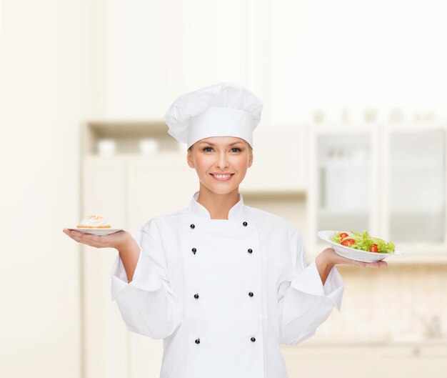 concetto di cucina e cibo - chef femminile sorridente, cuoco o fornaio con insalata e torta sui piatti