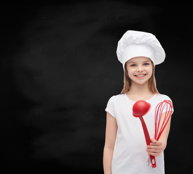 concetto di cucina e persone - bambina sorridente in cappello da cuoco con mestolo e frusta