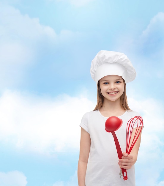 concetto di cucina e persone - bambina sorridente in cappello da cuoco con mestolo e frusta