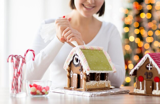 concetto di cucina, persone, natale e decorazione - donna felice che fa case di pan di zenzero a casa