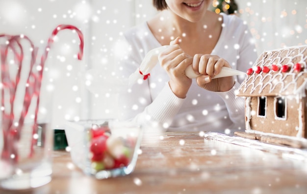 concetto di cucina, persone, natale e decorazione - donna felice che fa case di pan di zenzero a casa