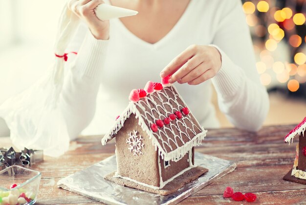 concetto di cucina, persone, natale e decorazione - primo piano di una donna felice che fa case di pan di zenzero a casa