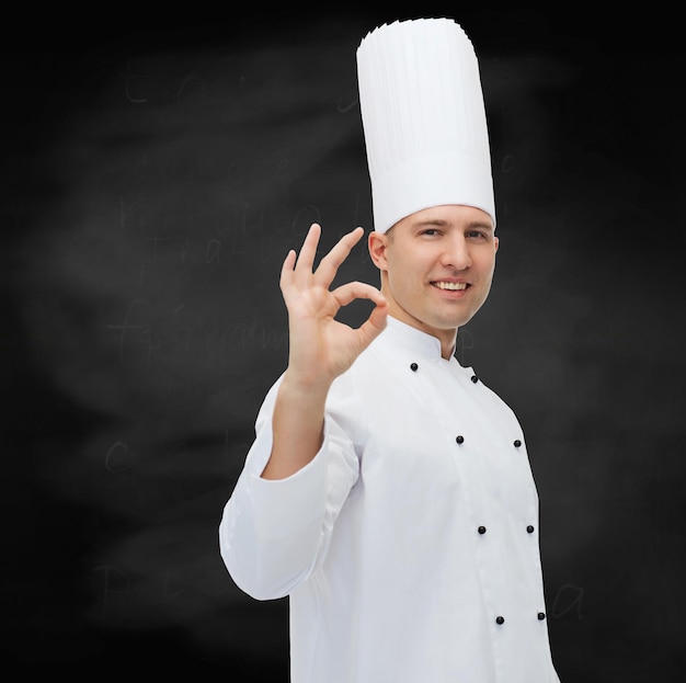 concetto di cucina, professione, gesto e persone - cuoco maschio felice che mostra ok segno su sfondo nero lavagna