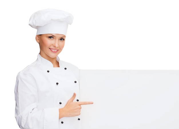 concetto di cucina, pubblicità e cibo - chef femminile sorridente, cuoco o fornaio che punta il dito sulla lavagna bianca