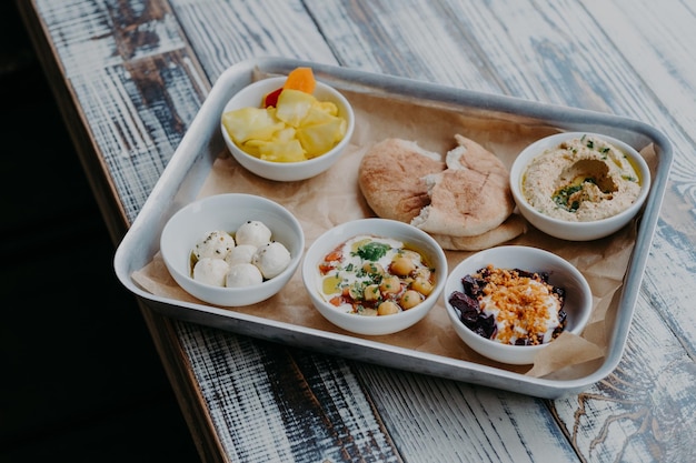 Concetto di cucina tradizionale israeliana Vista dall'alto di gustosi piatti esotici serviti su vassoio Verdure di pane pita su hummus di formaggio di capra alla griglia su tavolo di legno