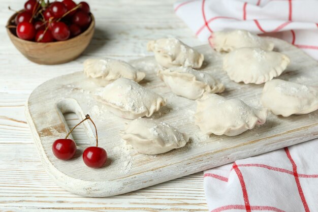 Concetto di cucinare pierogi con ciliegia sul tavolo di legno bianco