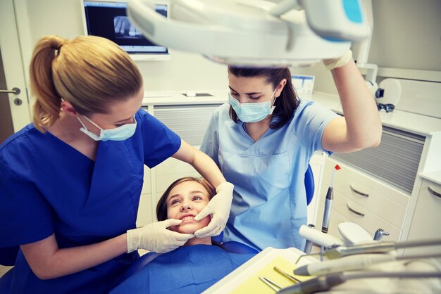 concetto di cura di persone, medicina, stomatologia e denti - dentista femminile felice con assistente che controlla i denti di occlusione dentale della ragazza del paziente presso l'ufficio della clinica dentale