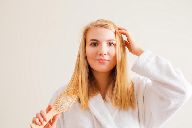 Concetto di cura e trattamento dei capelli Bella donna bionda che si spazzola i capelli in bagno