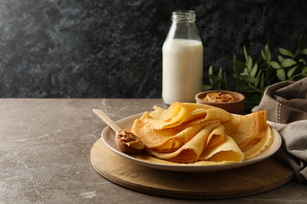 Concetto di deliziosa colazione con crepes con burro di arachidi e latte sul tavolo grigio