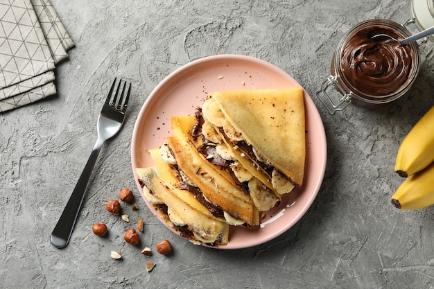 Concetto di deliziosa colazione con crepes con pasta di cioccolato, banana e noci su sfondo grigio