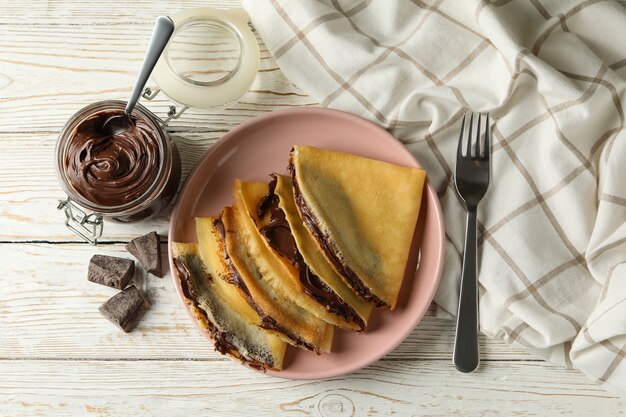 Concetto di deliziosa colazione con crepes con pasta di cioccolato su fondo di legno bianco