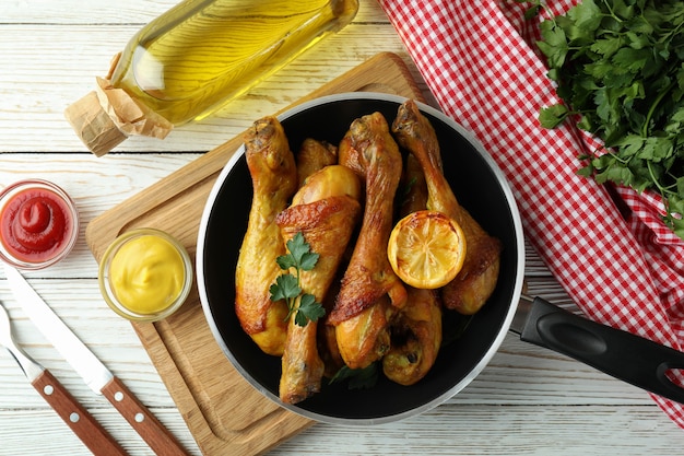 Concetto di delizioso mangiare con padella di cosce di pollo arrosto sul tavolo di legno bianco