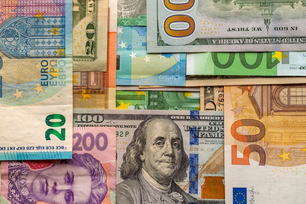 Concetto di denaro e finanze. Nuova fattura da cento dollari su sfondo colorato astratto di banconote in valuta nazionale ucraina, americana ed euro.