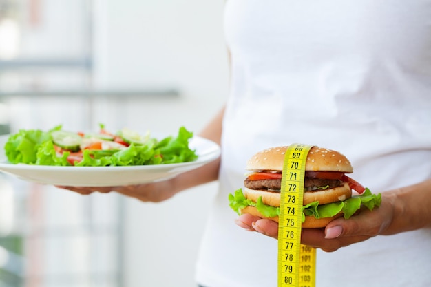 Concetto di dieta, donna che sceglie tra hamburger spazzatura e insalata fresca.