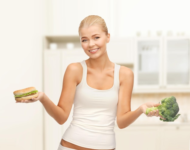 concetto di dieta e fitness - donna sportiva con broccoli e hamburger