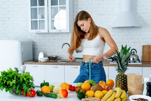 Concetto di dieta. Femmina in cucina con cibo sano. Frutta e verdura. Metro a nastro in vita.