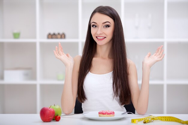 Concetto di dieta. Giovane donna che sceglie fra la frutta e i dolci