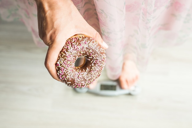 Concetto di dieta. Primo piano dei piedi della donna sulla bilancia con ciambella. Concetto di dolci, cibo spazzatura malsano e obesità.