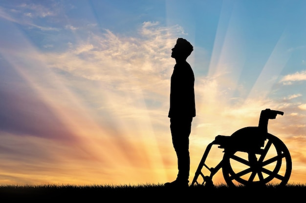 Concetto di disabilità e malattia. Silhouette di una persona disabile che si distingueva dalla sedia a rotelle sullo sfondo del tramonto