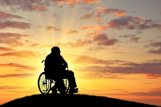 Concetto di disabilità e vecchiaia. Sagoma di persona disabile in sedia a rotelle sullo sfondo del tramonto