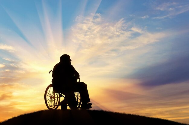 Concetto di disabilità e vecchiaia. Sagoma di persona disabile in sedia a rotelle sullo sfondo del tramonto